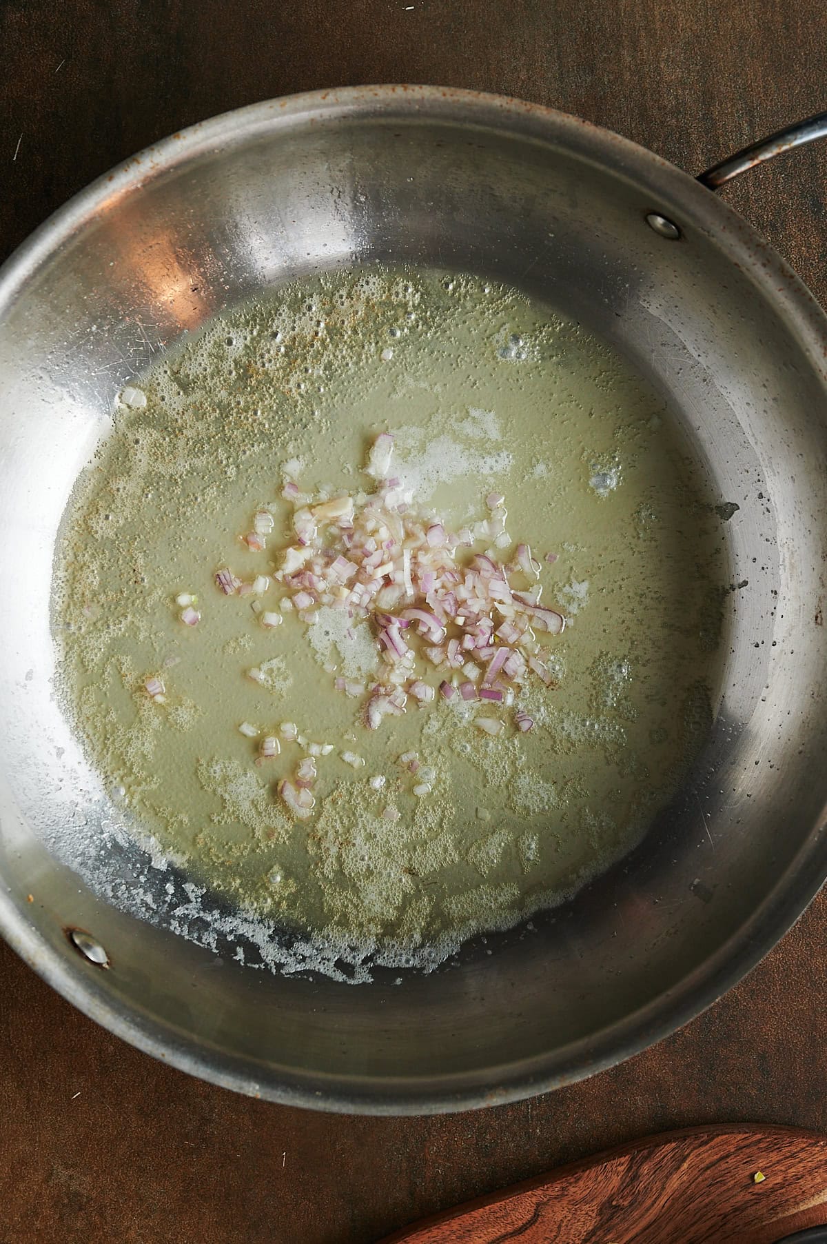 Shallots being sauteed in butter in a skillet on a brown background.
