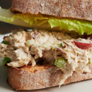 A close-up of a chicken salad sandwich on crusty bread with lettuce. The chicken salad contains pieces of grape and appears creamy.