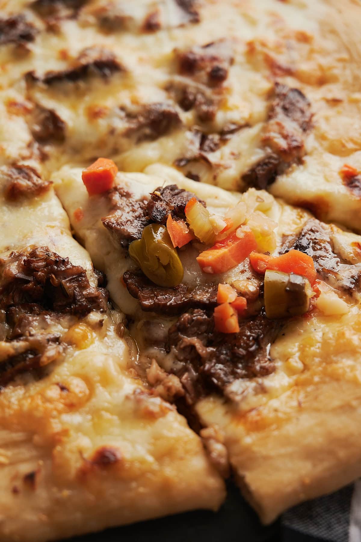 A close-up of a cheese pizza with browned crust and melted cheese, topped with pieces of cooked meat and a mixture of giardiniera on one slice.
