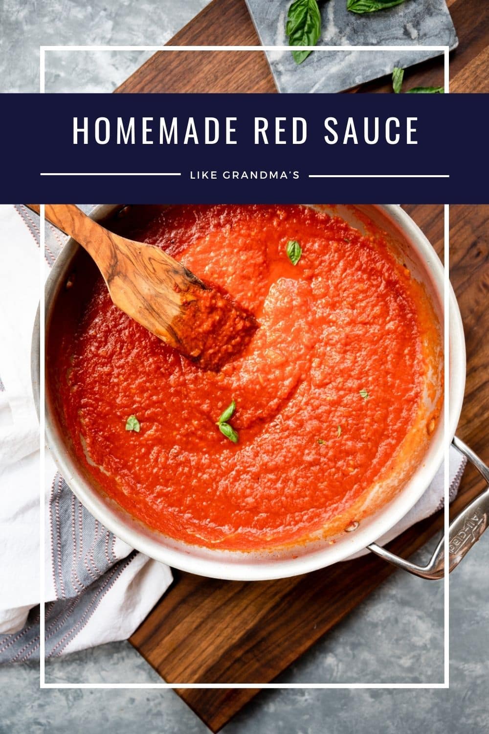 A saucepan filled with red tomato sauce sits on a round wooden board. A wooden spoon rests in the sauce, and a small basil leaf garnishes the top. Text overlay reads “Homemade Red Sauce Like Grandma’s.”.