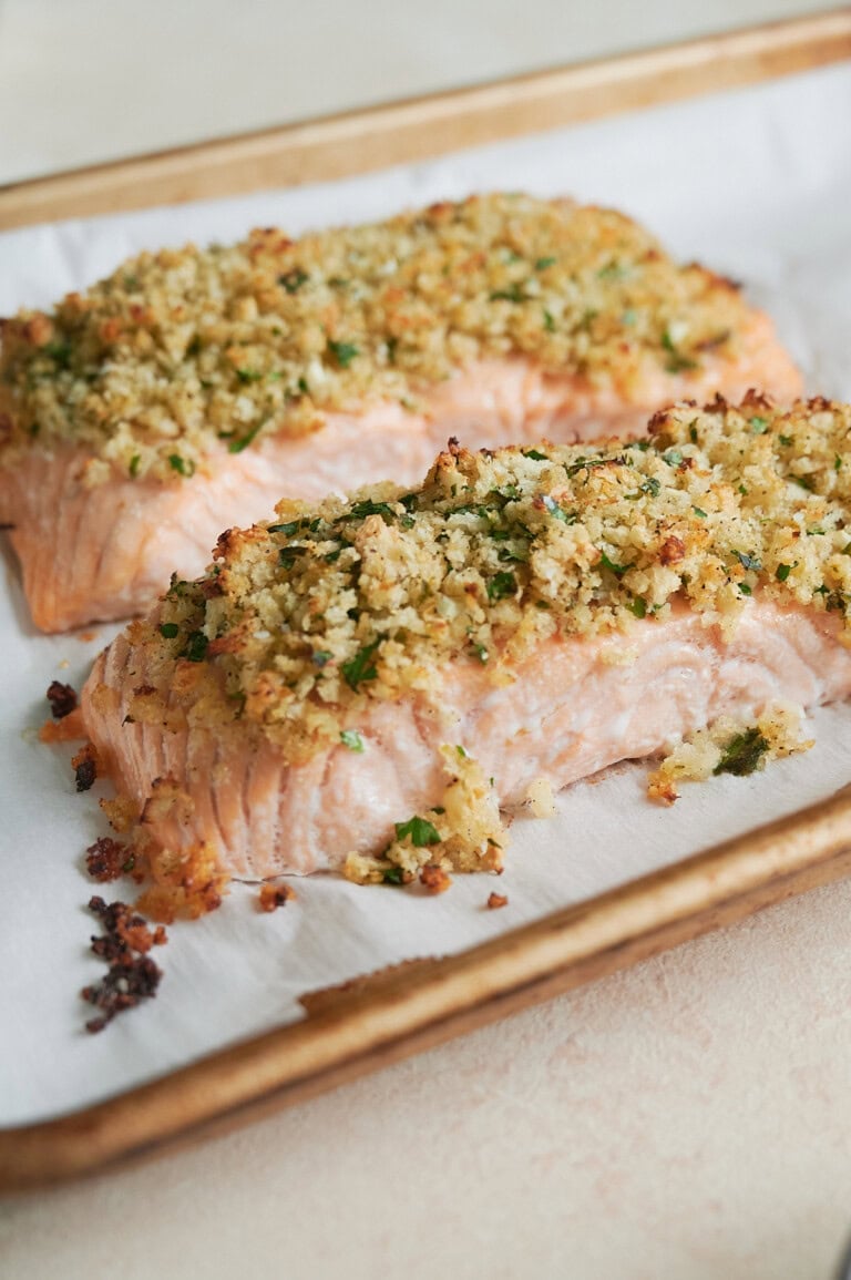 Two baked salmon fillets topped with a golden, crispy herb and breadcrumb crust on a parchment-lined baking sheet.