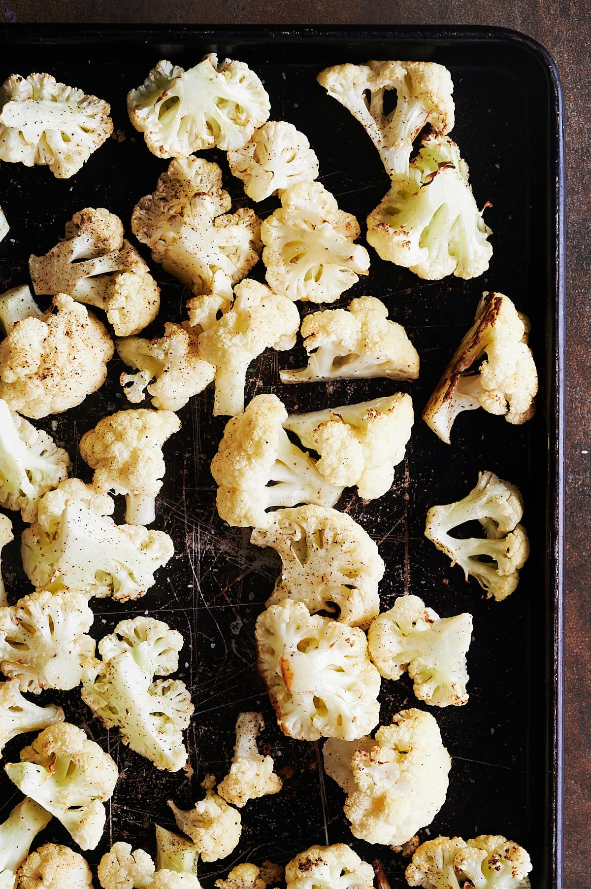 A baking sheet covered with evenly spread roasted cauliflower florets.