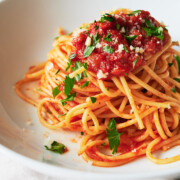 A pasta bowl of spaghetti topped with tomato sauce, grated cheese, and fresh parsley.