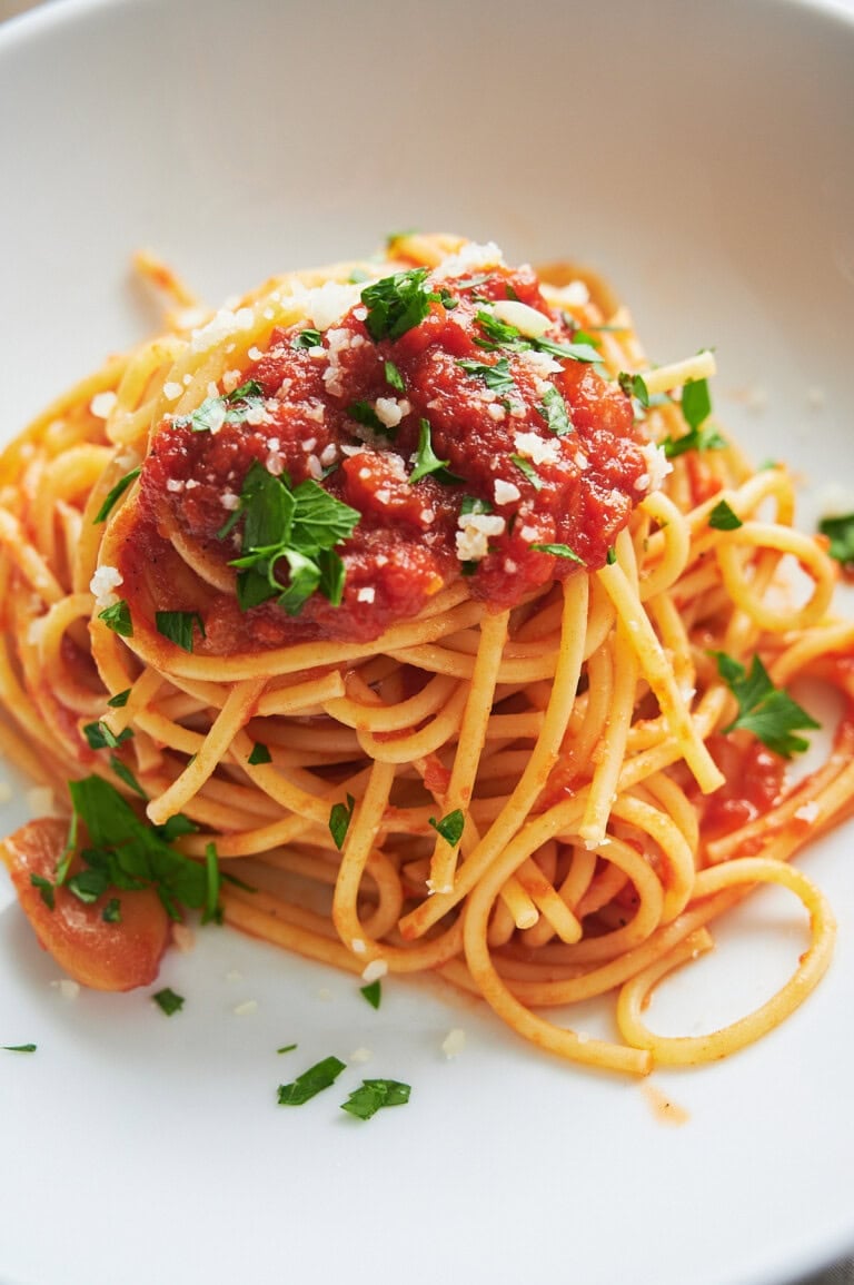 A plate of spaghetti topped with tomato gravy, grated cheese, and chopped parsley on a white dish.