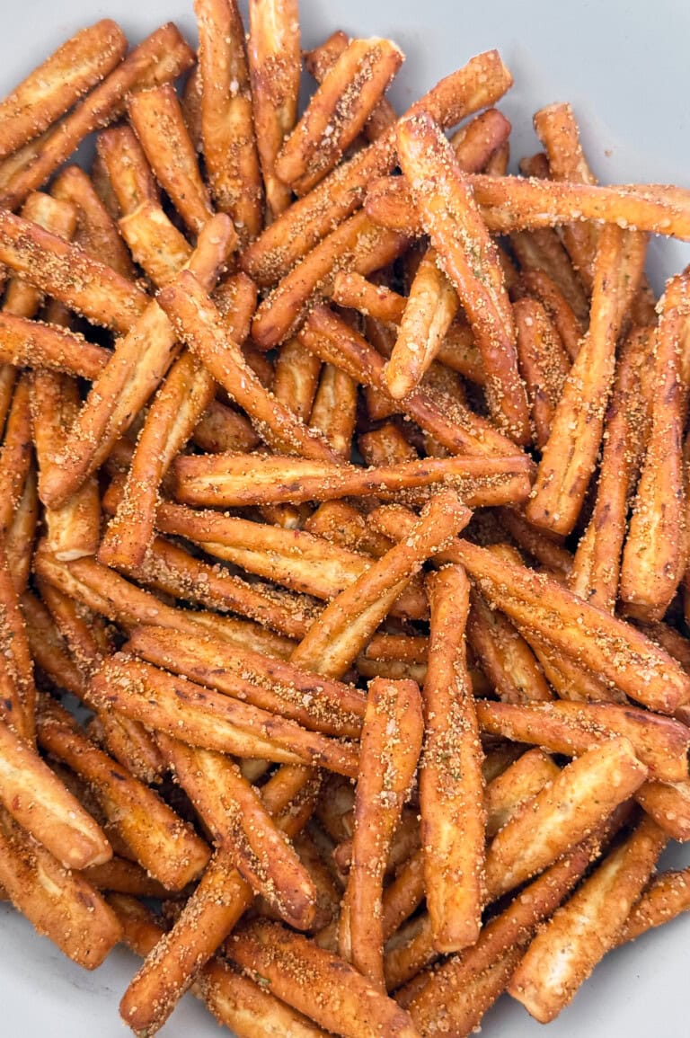 A bowl filled with seasoned pretzel sticks, coated with visible spices and arranged closely together.
