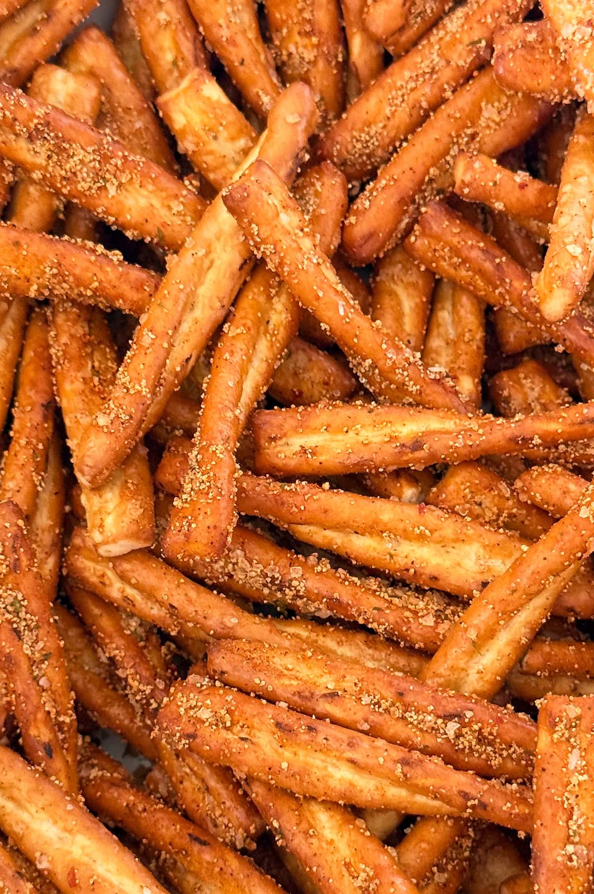 Close-up view of a pile of seasoned pretzel sticks, coated with visible grains of seasoning.