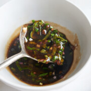 A spoon holds a mixture of basil vinaigrette over a white bowl.