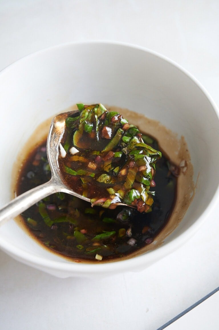 A spoon holds a mixture of basil vinaigrette over a white bowl.