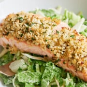 A piece of baked salmon with a breadcrumb and herb crust served on a bed of green salad with a creamy dressing.