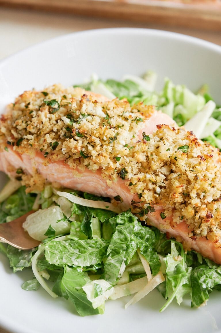 A piece of baked salmon with a breadcrumb and herb crust served on a bed of green salad with a creamy dressing.
