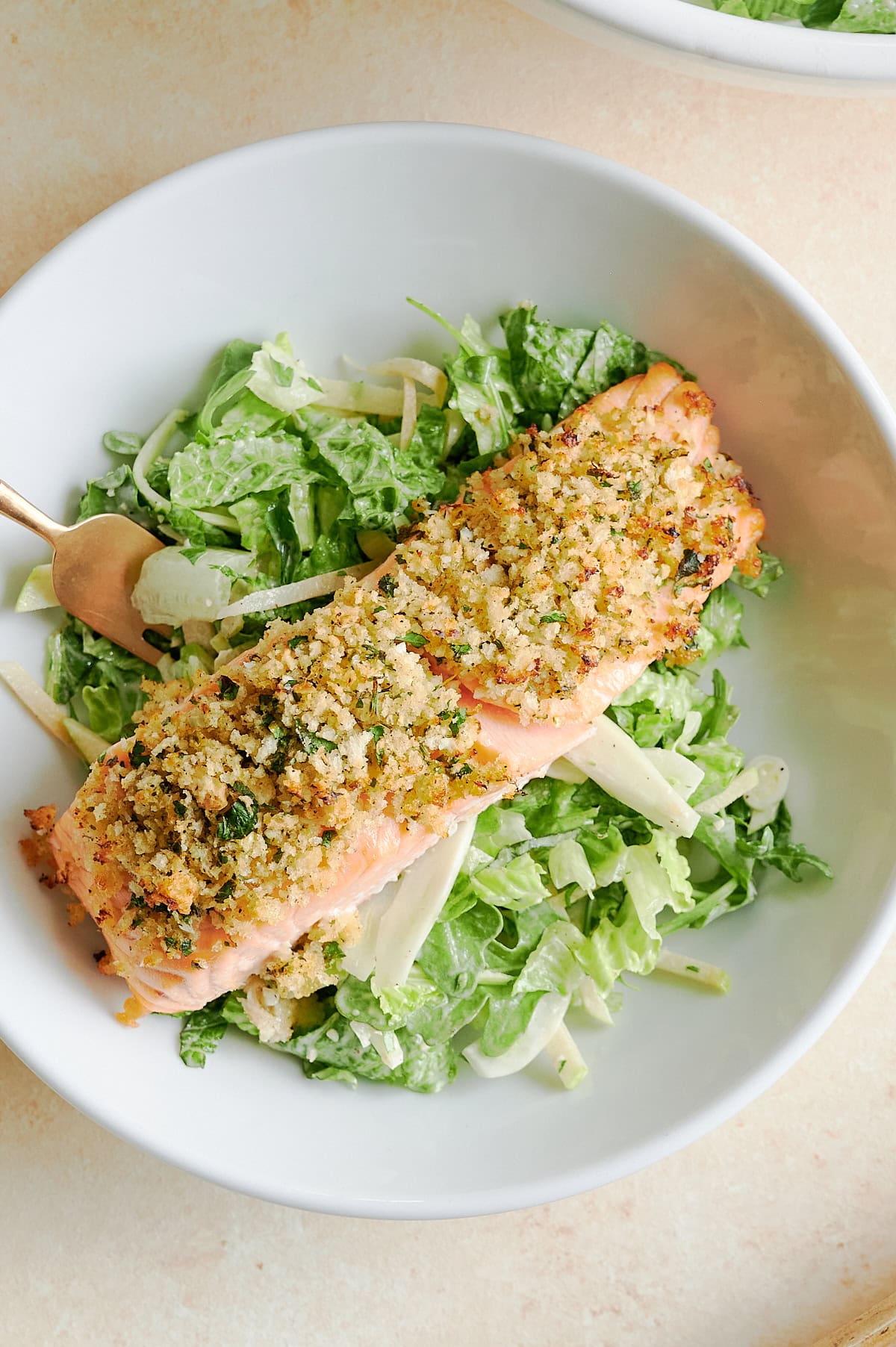 A plate with a piece of herb-crusted salmon served on a bed of creamy salad greens and fennel, with a fork on the side.