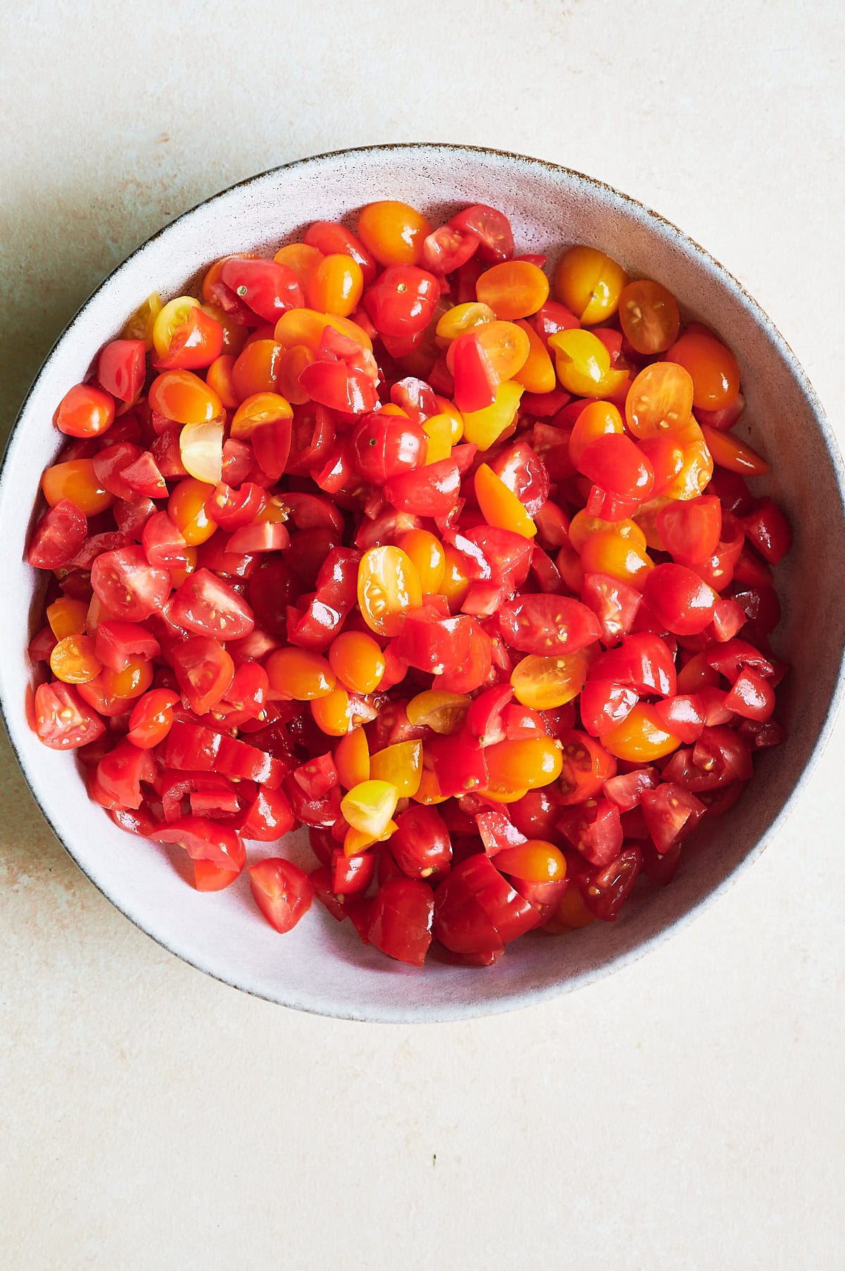 A bowl filled with chopped red and yellow cherry tomatoes on a light-colored surface for bruschetta.