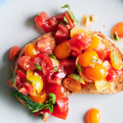 Two slices of toasted bread topped with diced red and yellow tomatoes and fresh basil on a blue-rimmed plate.