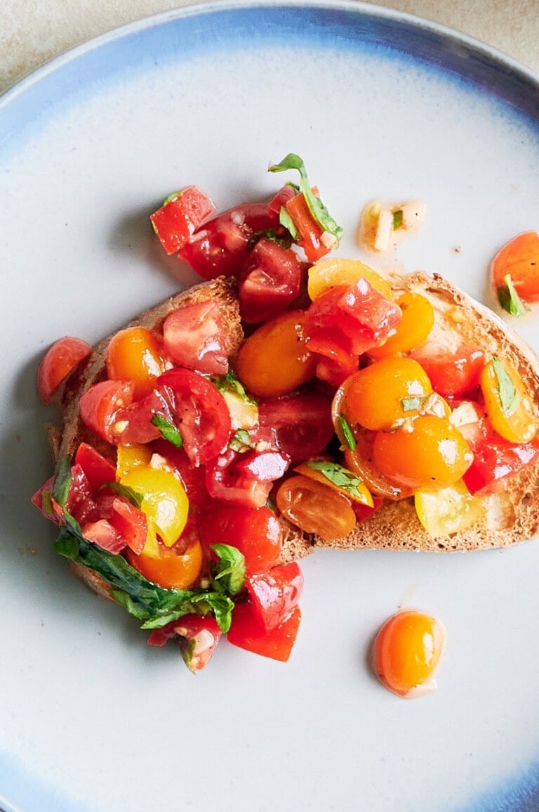 Two slices of toasted bread topped with diced red and yellow tomatoes and fresh basil on a blue-rimmed plate.