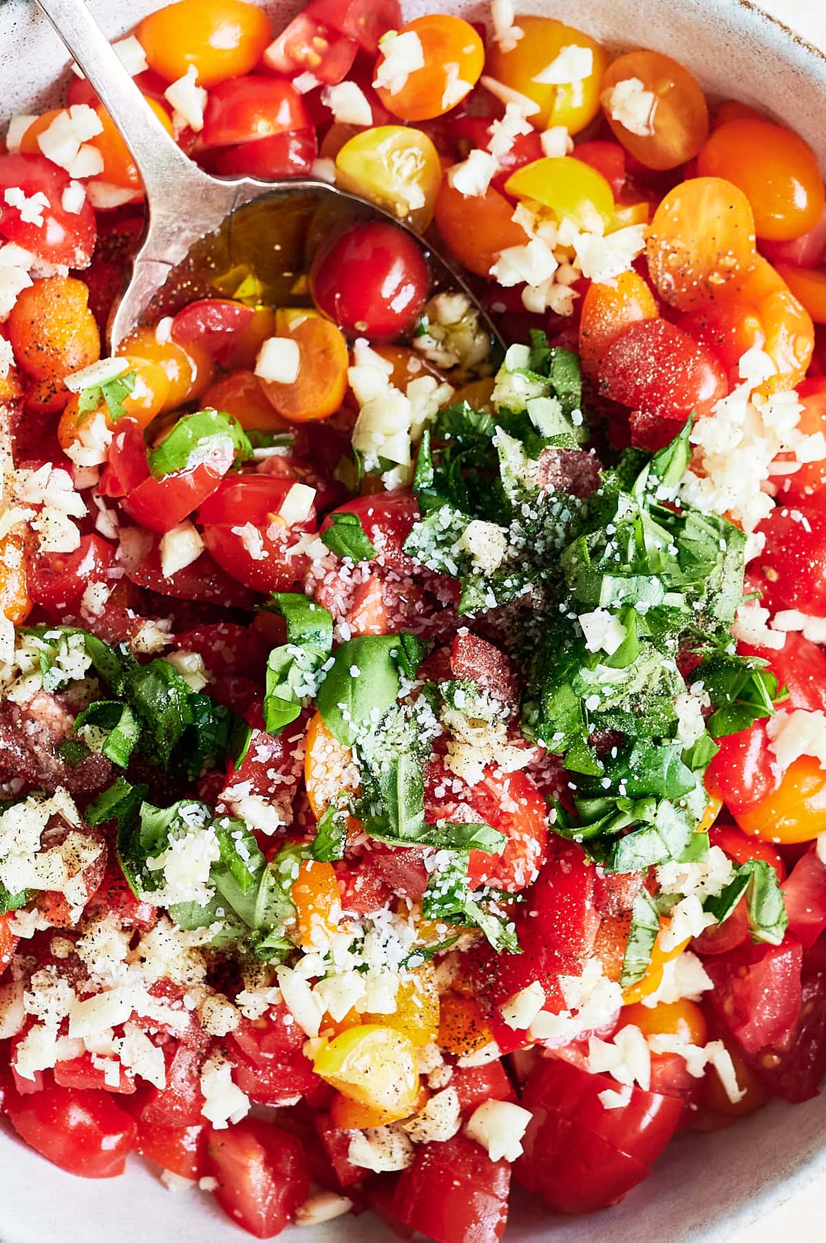 A bowl of chopped red and yellow tomatoes, fresh basil, minced garlic, and black pepper with a spoon for bruschetta.