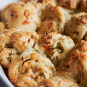 Golden brown cheesy garlic bread rolls in a white baking dish, with melted cheese and herbs visible on the flaky, baked surface.