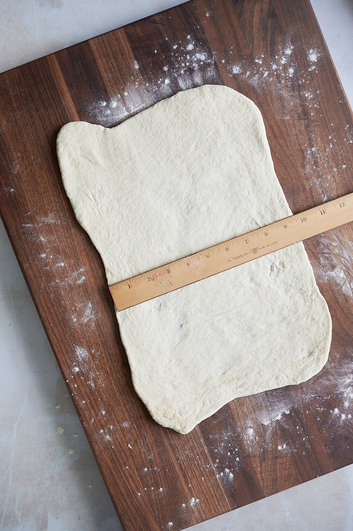 Rectangular piece of dough on a floured wooden board, with a ruler placed across the middle for measurement.
