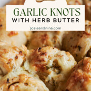 Close-up of cheesy garlic knots topped with herbs and melted cheese, with a label reading Cheesy Garlic Knots with Herb Butter and a website link.