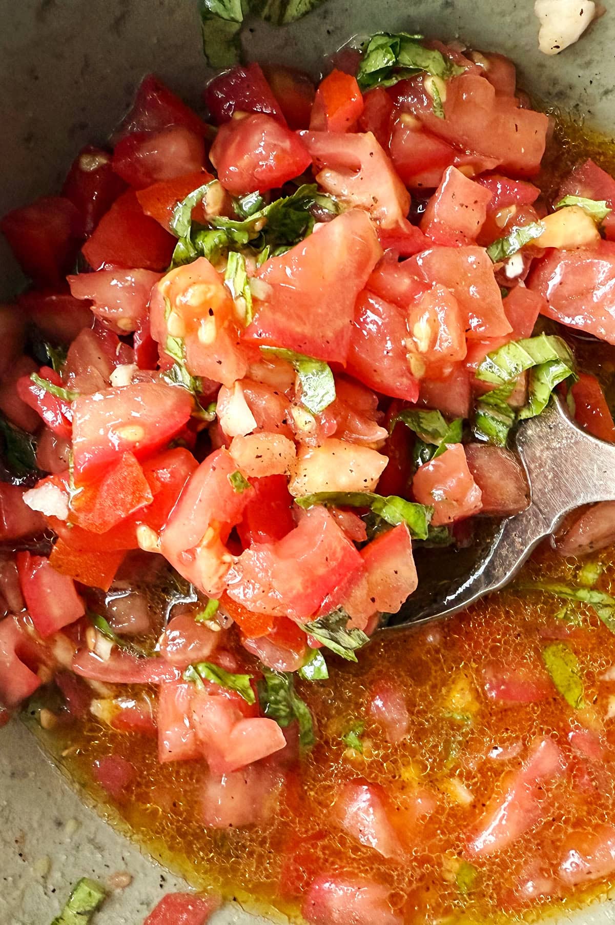 Close-up of bruschetta with chopped tomatoes, basil, and seasoning mixed with olive oil and liquid in a bowl.