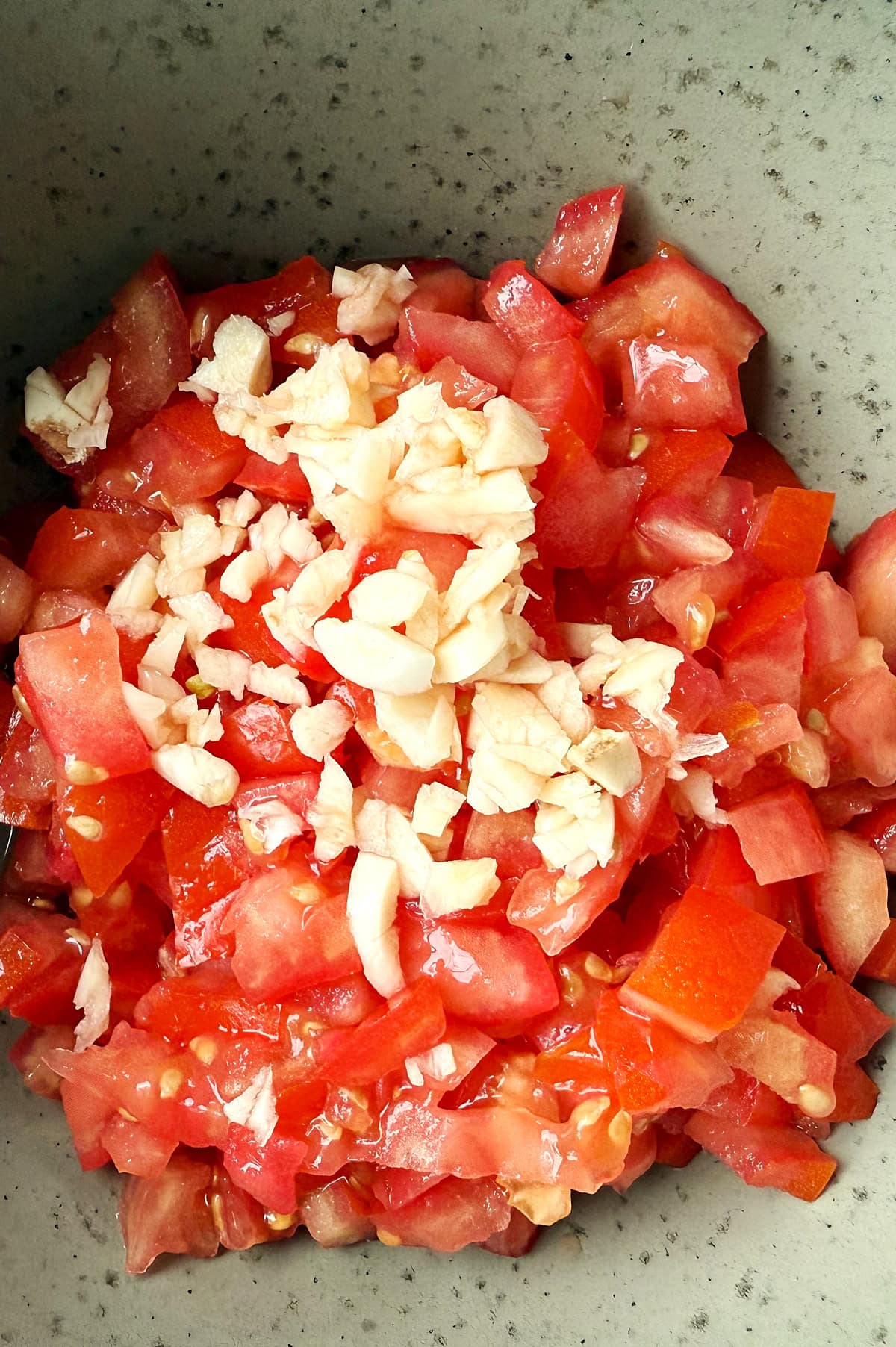 Chopped tomatoes and minced garlic in a speckled bowl for bruschetta.