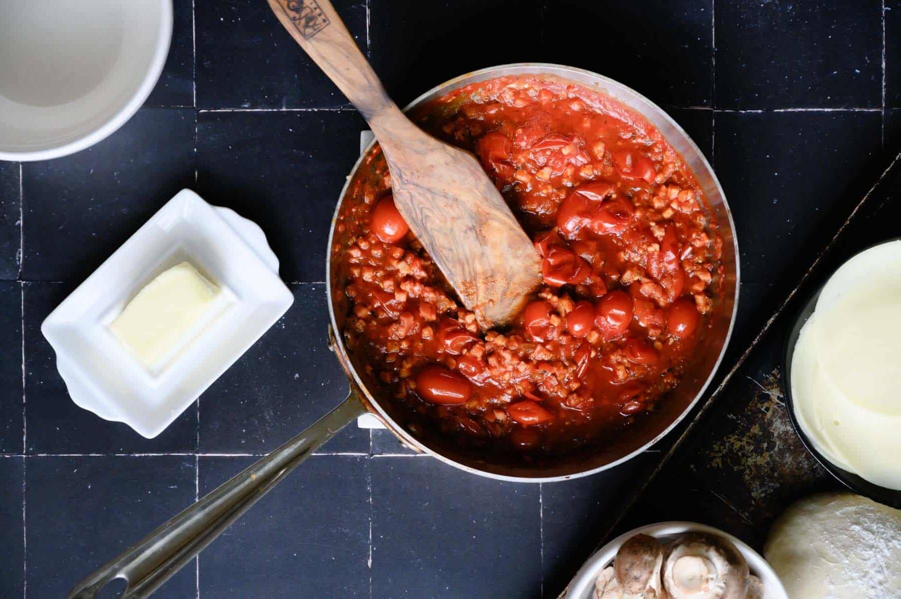 pizza sauce in a skillet with a wooden paddle.