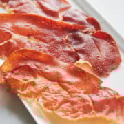 Three slices of crispy prosciutto are arranged on a rectangular white plate.