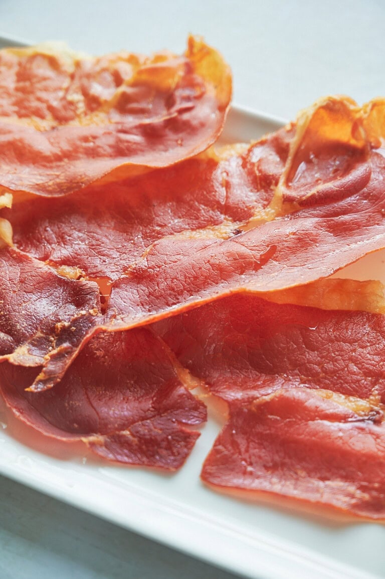 Several slices of crispy prosciutto are arranged on a white rectangular plate.