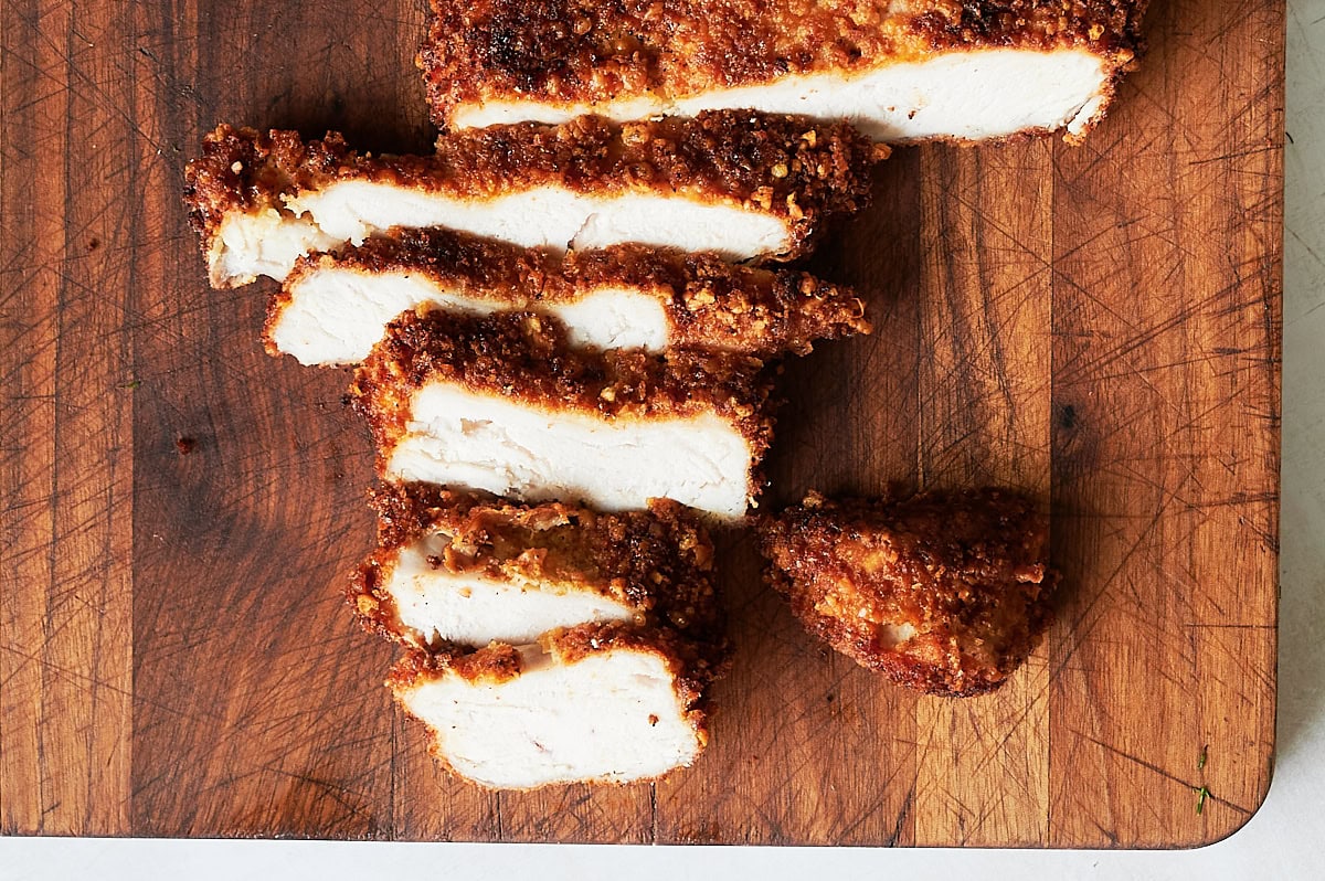 Slices of breaded and fried chicken breast are arranged on a wooden cutting board.