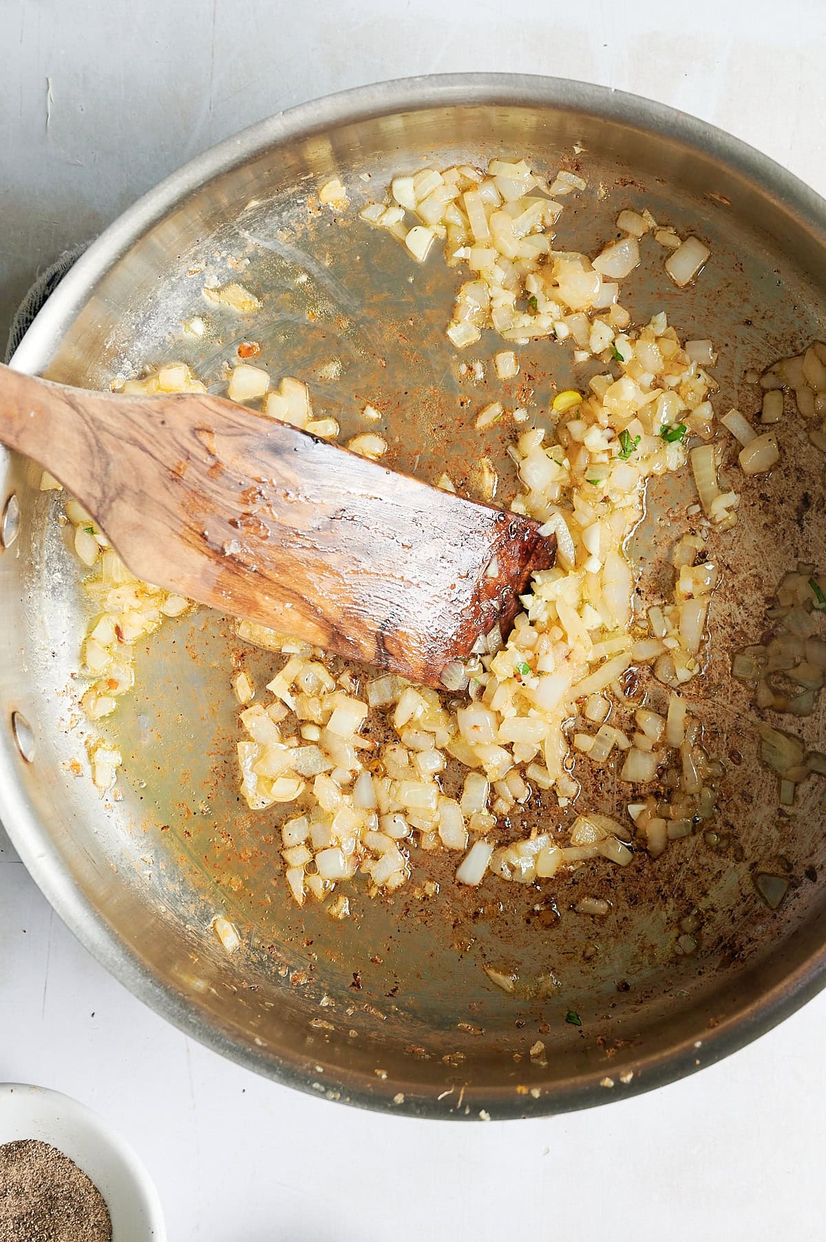 Chopped onions being sautéed in a stainless steel pan with a wooden spatula; browned bits are visible on the pan’s surface.