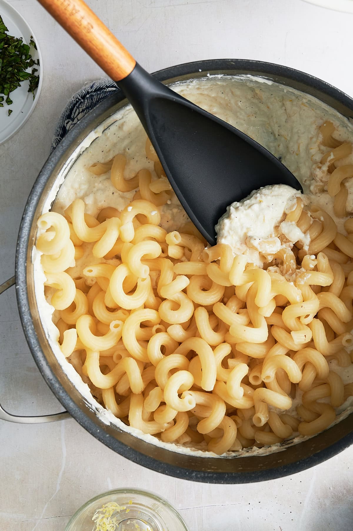 Cooked cavatappi pasta in a pot with creamy white sauce, being stirred with a black spatula.