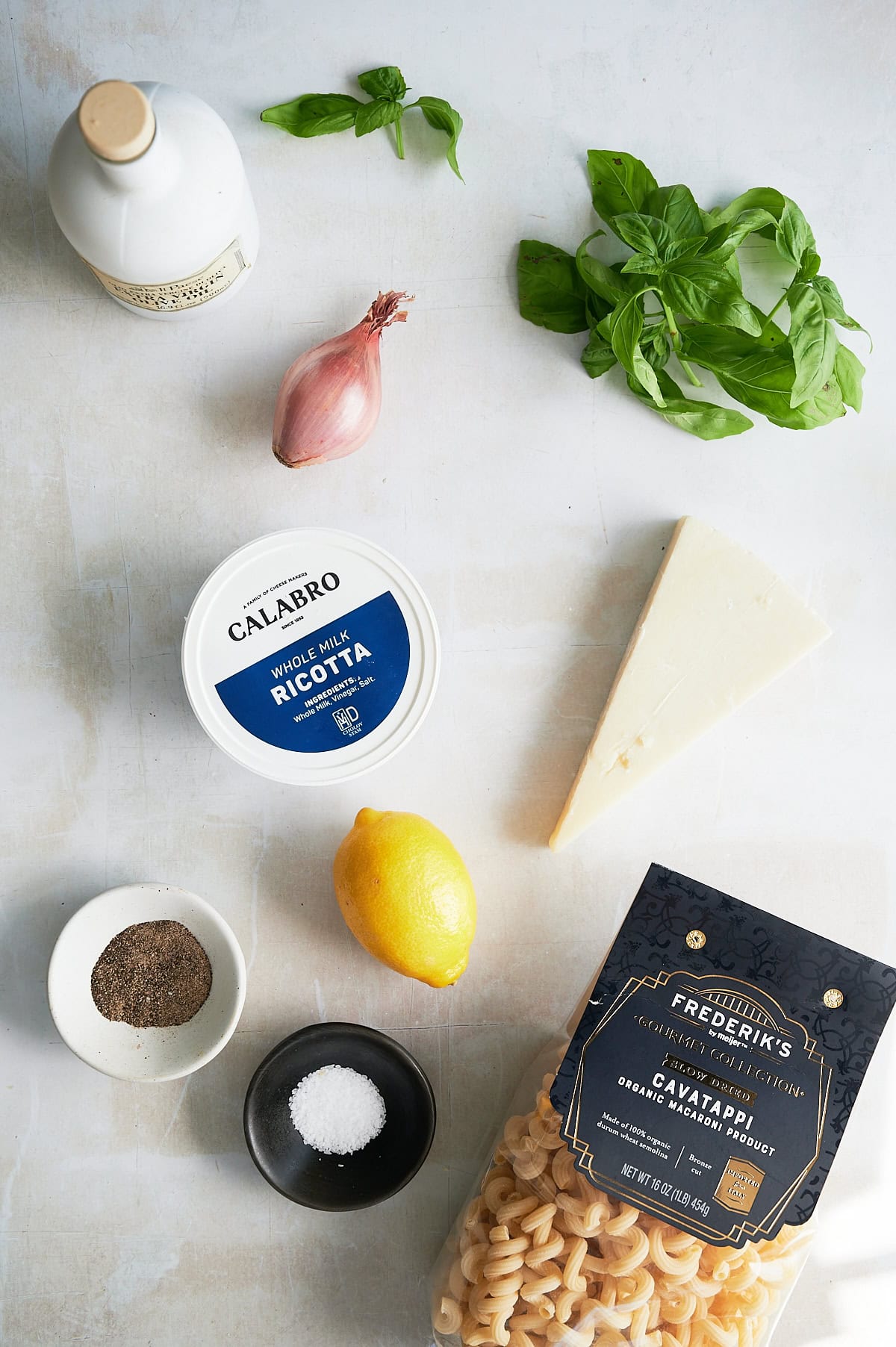 Pasta, ricotta, parmesan wedge, lemon, shallot, fresh basil, olive oil, salt, and pepper arranged on a light surface.