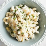 A bowl of creamy lemon ricotta fusilli topped with chopped herbs and grated cheese, served in a decorative light blue bowl.