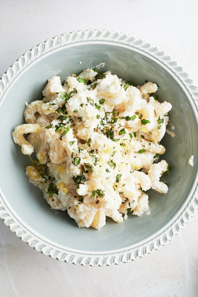 A bowl of creamy lemon ricotta fusilli topped with chopped herbs and grated cheese, served in a decorative light blue bowl.