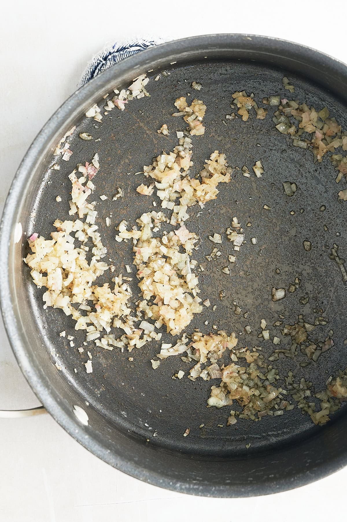 Chopped onions being sautéed in a large metal pan, with some bits starting to brown.