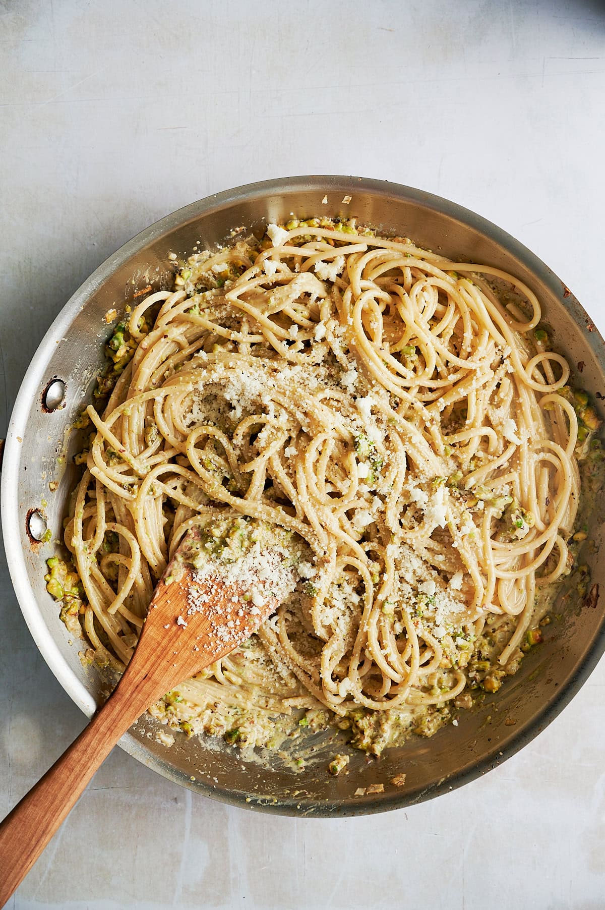 A pan of cooked spaghetti mixed with grated cheese and a creamy sauce, with a wooden spoon partially stirring the pasta.
