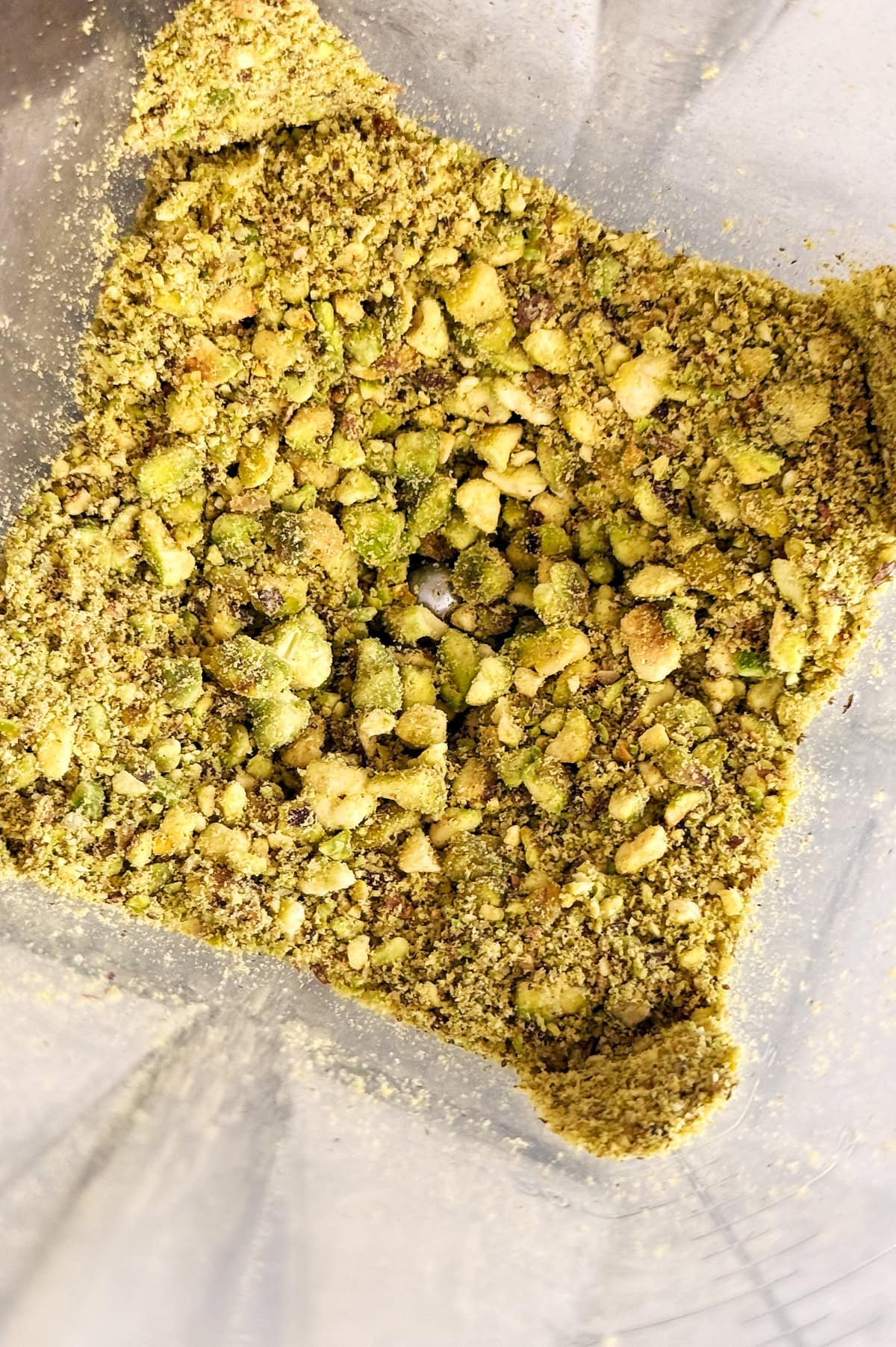 Coarsely ground pistachios in a blender container, showing a mixture of small chunks and fine powder.