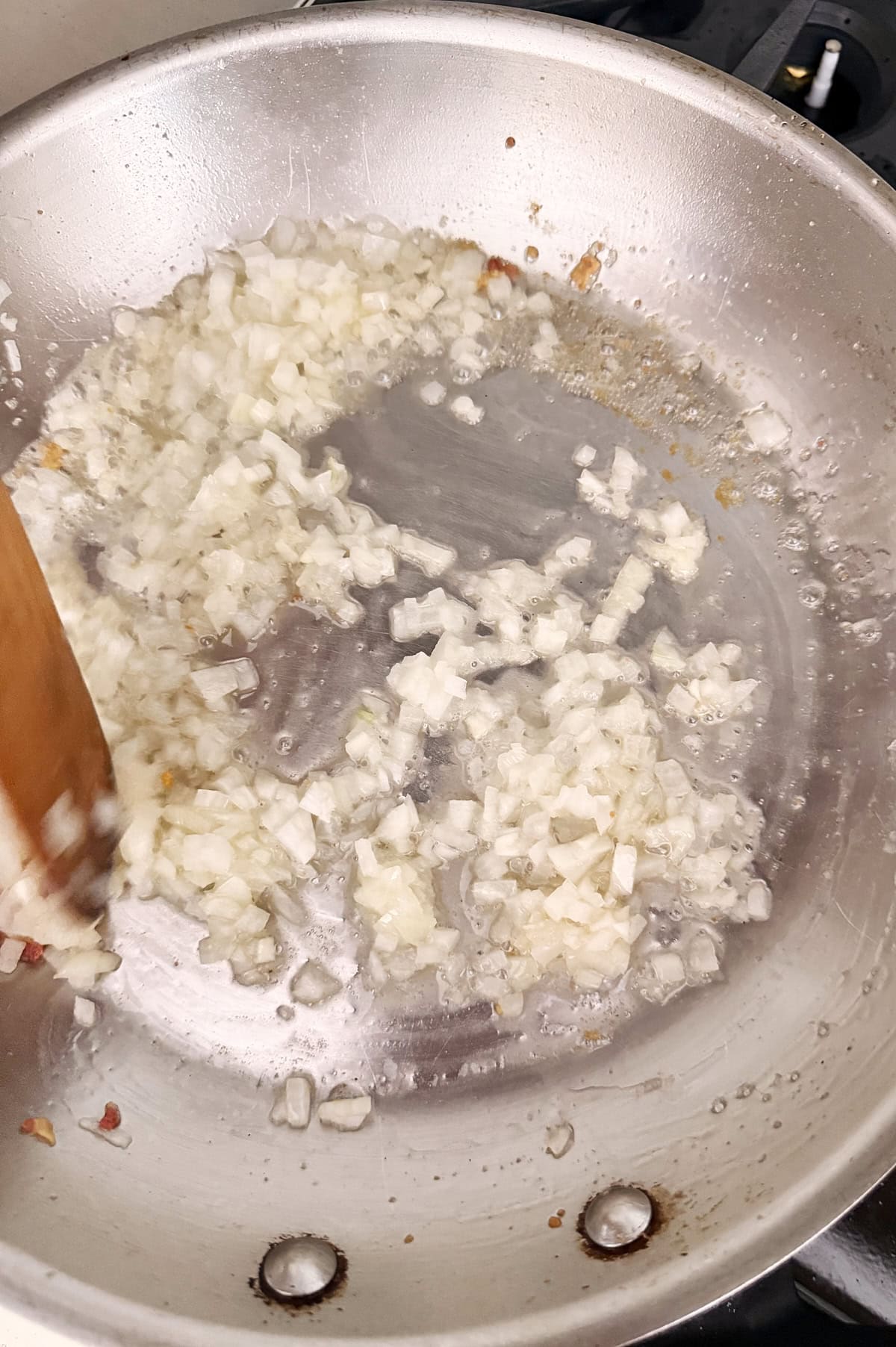 Chopped onions being sautéed in a stainless steel pan with a wooden spatula.