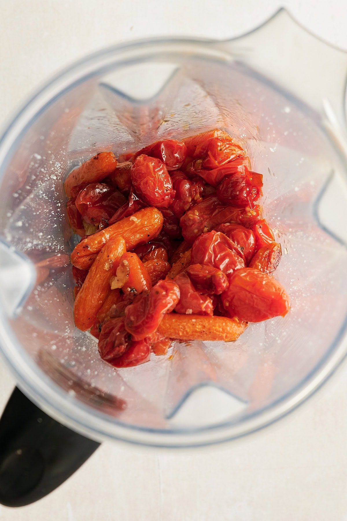 Roasted tomatoes and carrots inside a blender, ready to be blended.