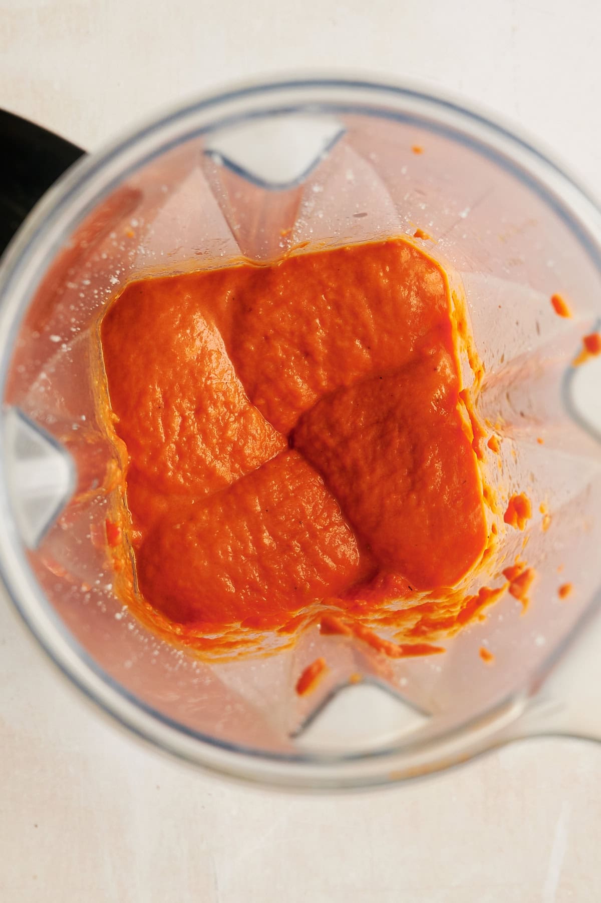 A top-down view of a blender containing smooth, blended orange-red tomato pasta sauce.