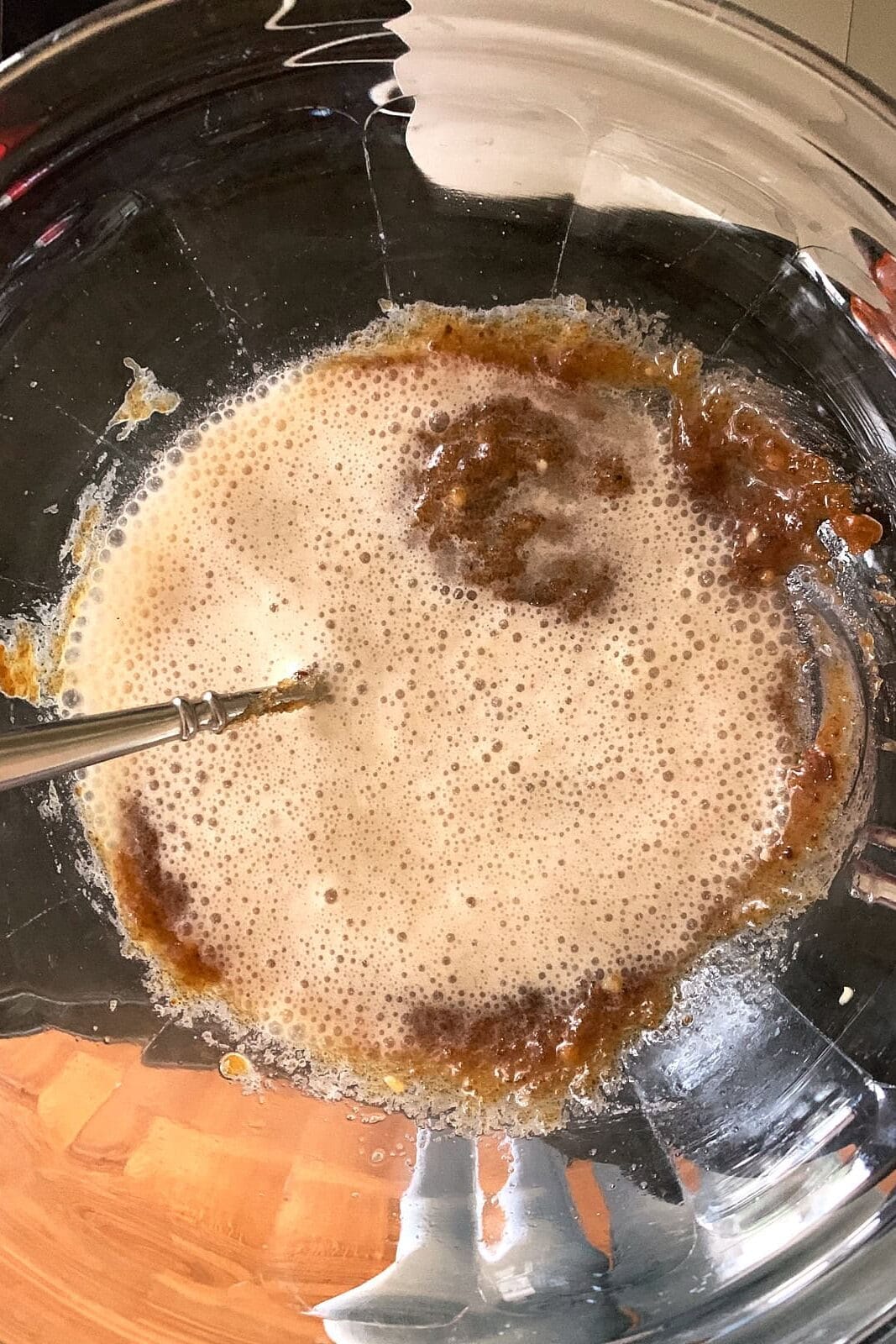 A metal whisk in a glass bowl containing a bubbly brown sugar mustard ham glaze.