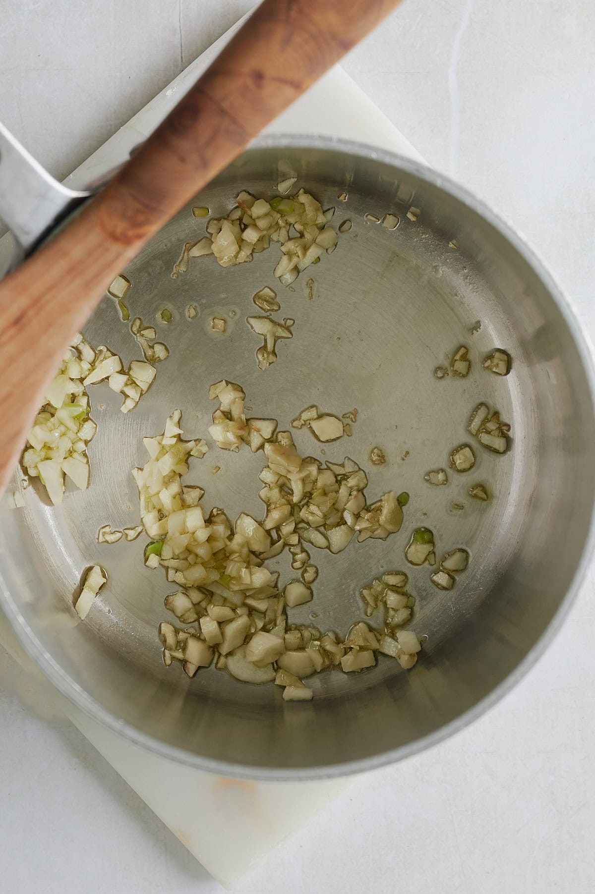 Chopped onions are sautéing in a stainless steel pot, with a wooden-handled utensil resting on the edge.