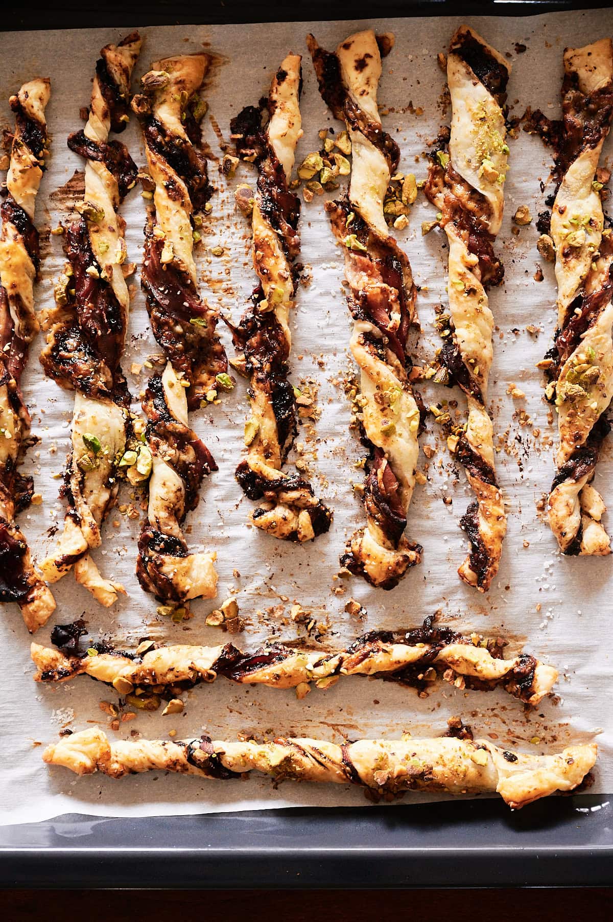 Baked puff pastry twists with a fig and pistachio filling arranged on a parchment-lined baking sheet.