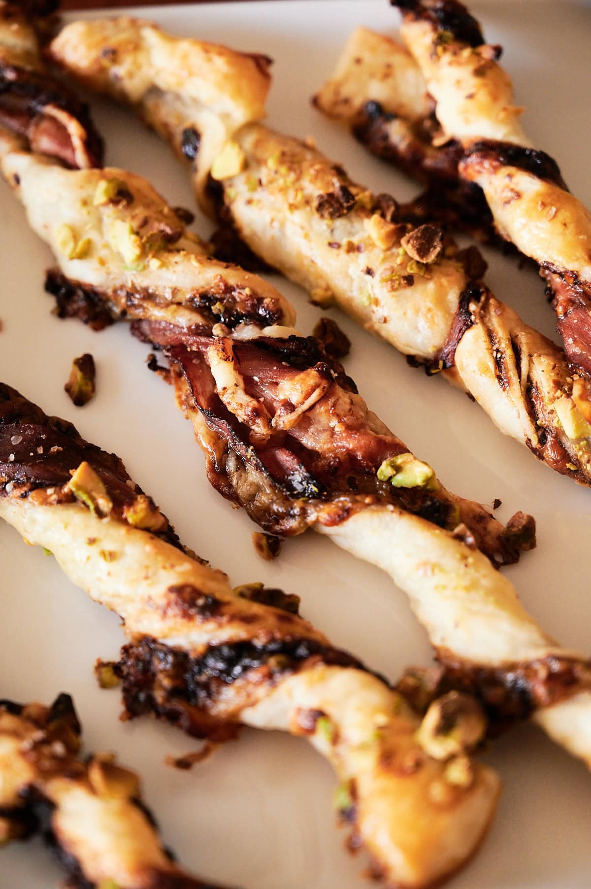 Close-up of twisted puff pastry straws with visible layers of dough, fig jam, and pistachios on a white surface.
