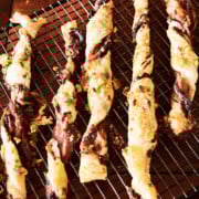 Several twisted puff pastry straws with fig filling rest on a cooling rack atop a wooden surface.