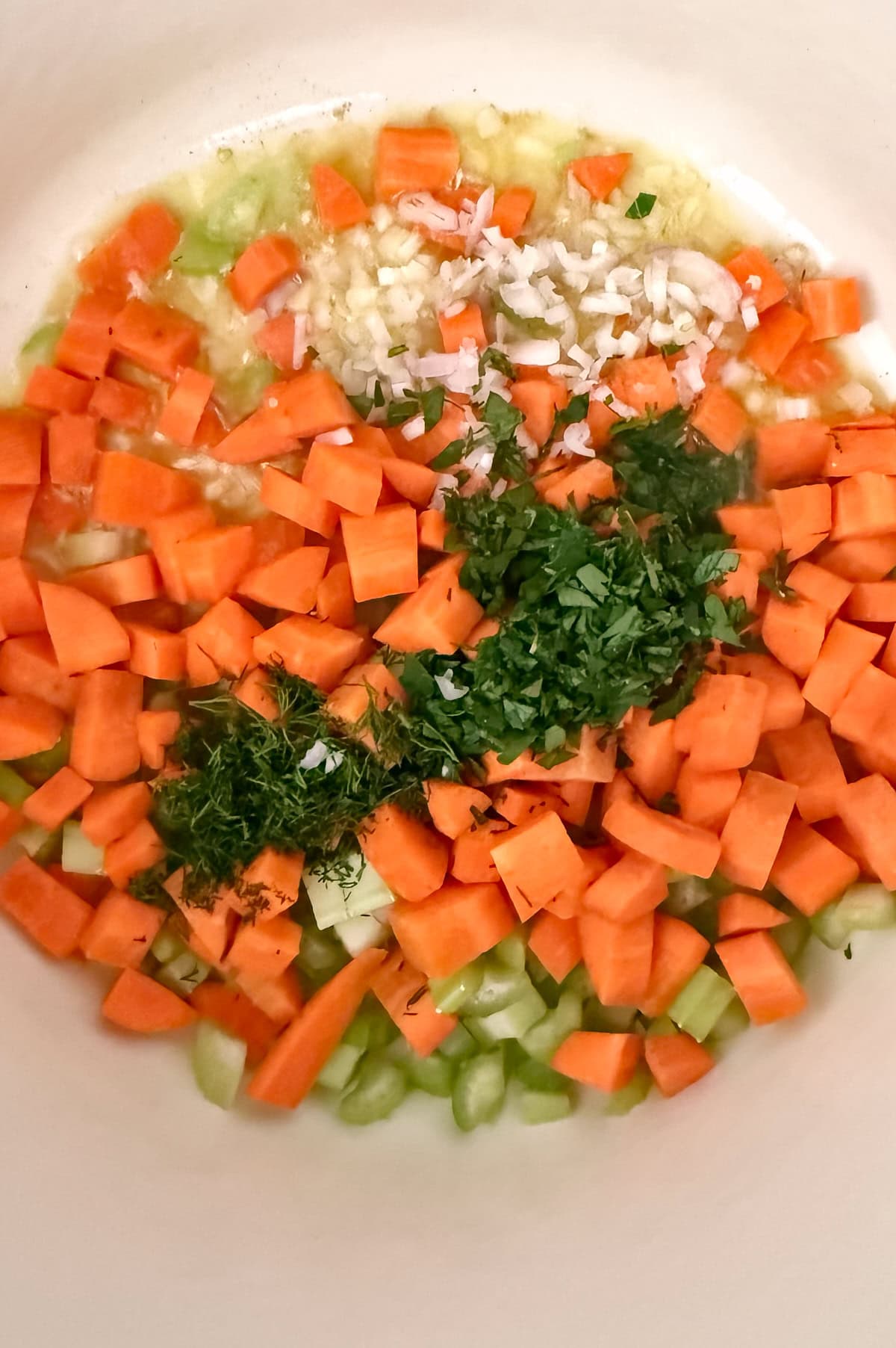 Chopped carrots, celery, onion, garlic, and fresh herbs being sauteed in a pot for farro soup.
