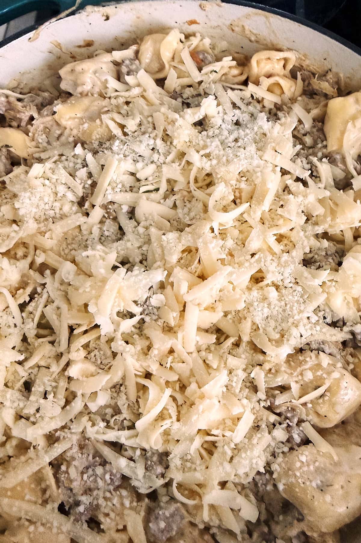 A close-up of uncooked tortellini covered with shredded cheese in a white pan.