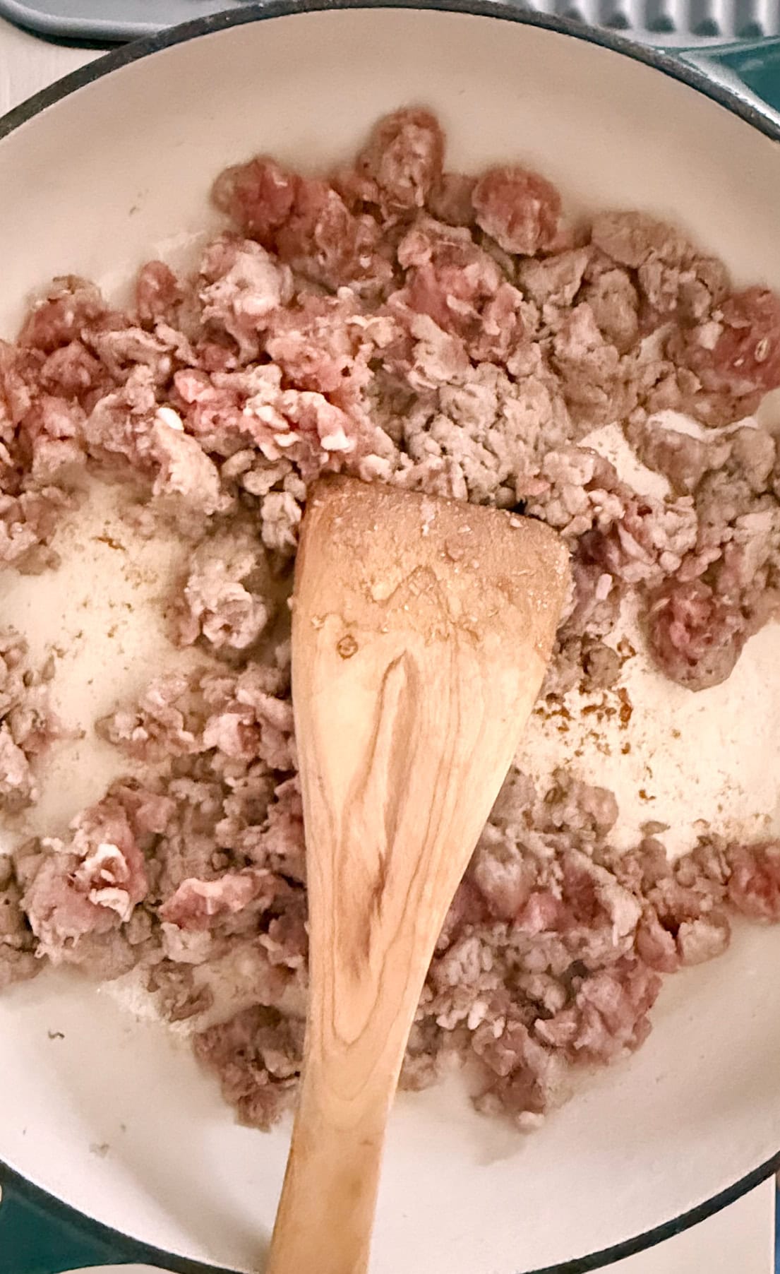 Ground sausage being browned in a pan with a wooden spatula for stirring.
