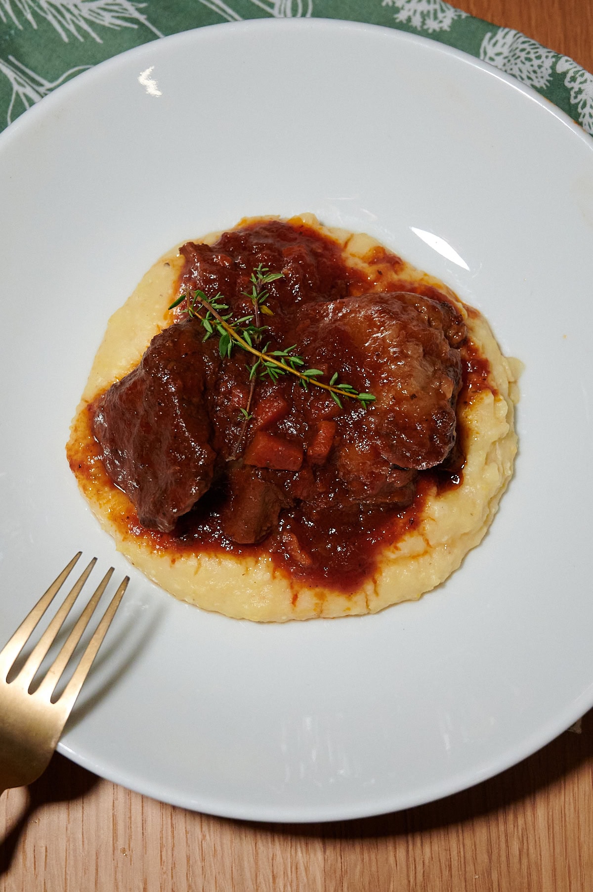 Beef short rib ragu served on creamy polent, garnished with fresh thyme, presented on a white bowl.