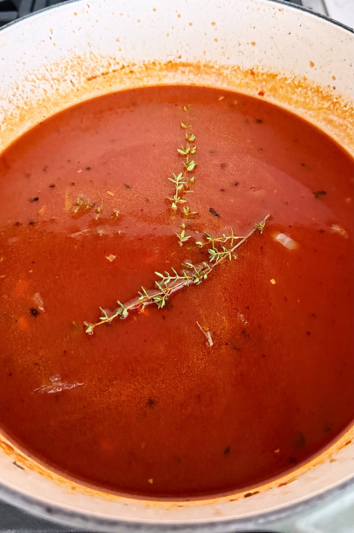 A pot of beef short ribs simmering on a stove, garnished with sprigs of fresh thyme floating on the surface.