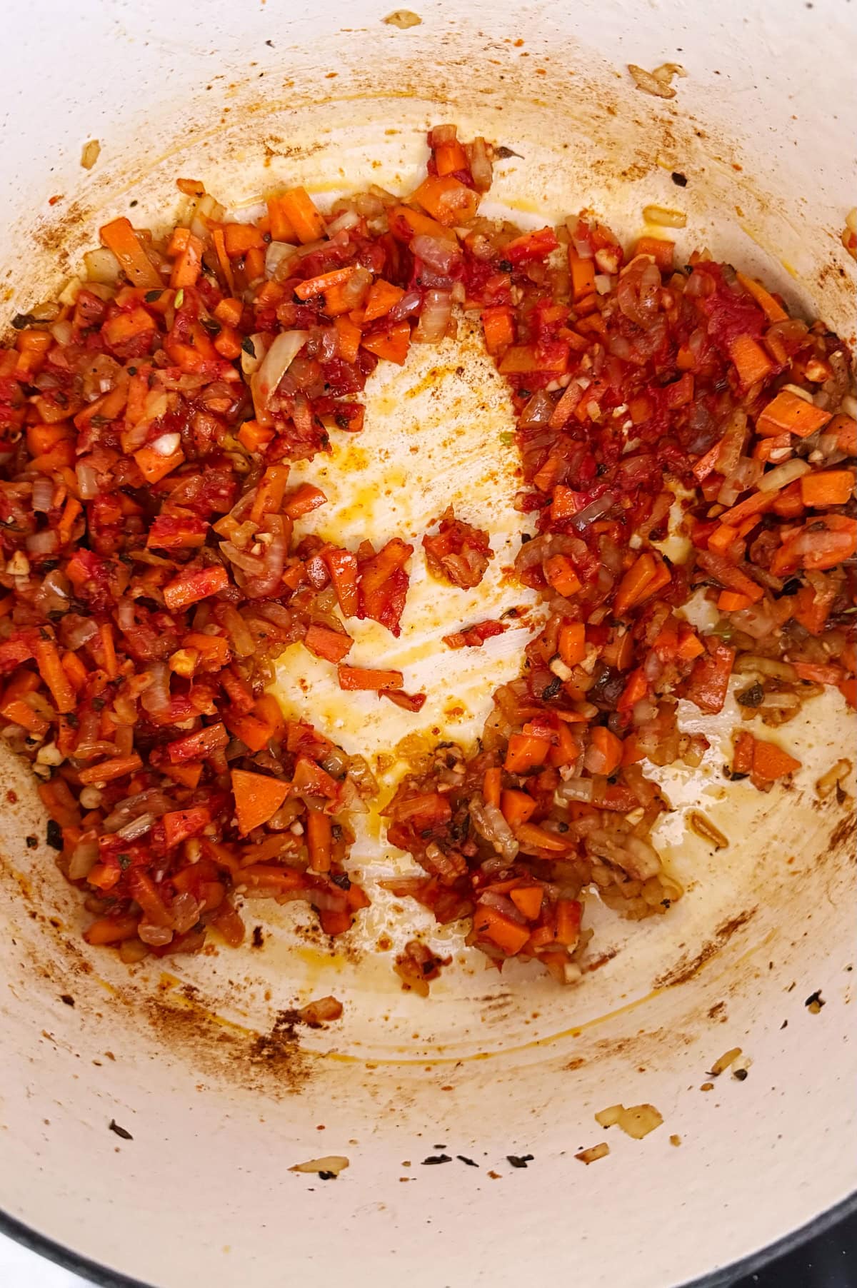 Chopped onions, carrots, and tomato pasta caramelizing in a white pot.